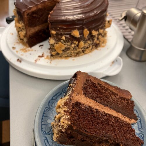 Cut chocolate cake with chocolate buttercream, chocolate ganache, and cookie crumble laying on a plate