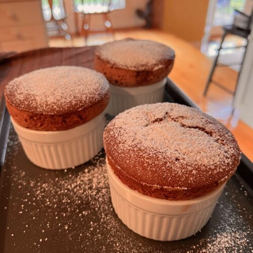 freshly baked chocolate souffle in white ramekins with powdered sugar on top