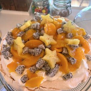 pavlova dessert with peaches, star fruit, dragon fruit, and whipped cream on a glass cake stand